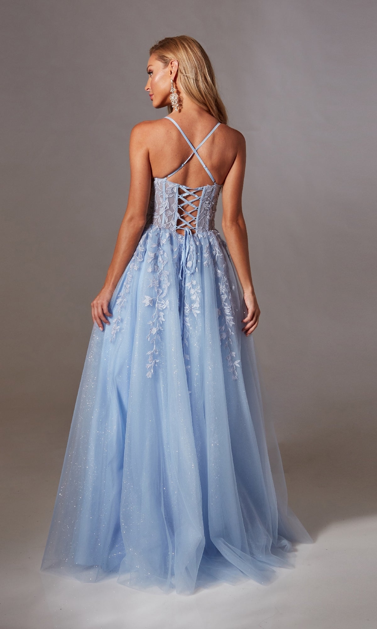 A woman poses against a neutral backdrop in the Aerie Couture 266 Lace-Up Long Prom Ball Gown, featuring embroidered lace, crisscross straps, floral details, an open lace-up back, and a flowing tulle skirt.